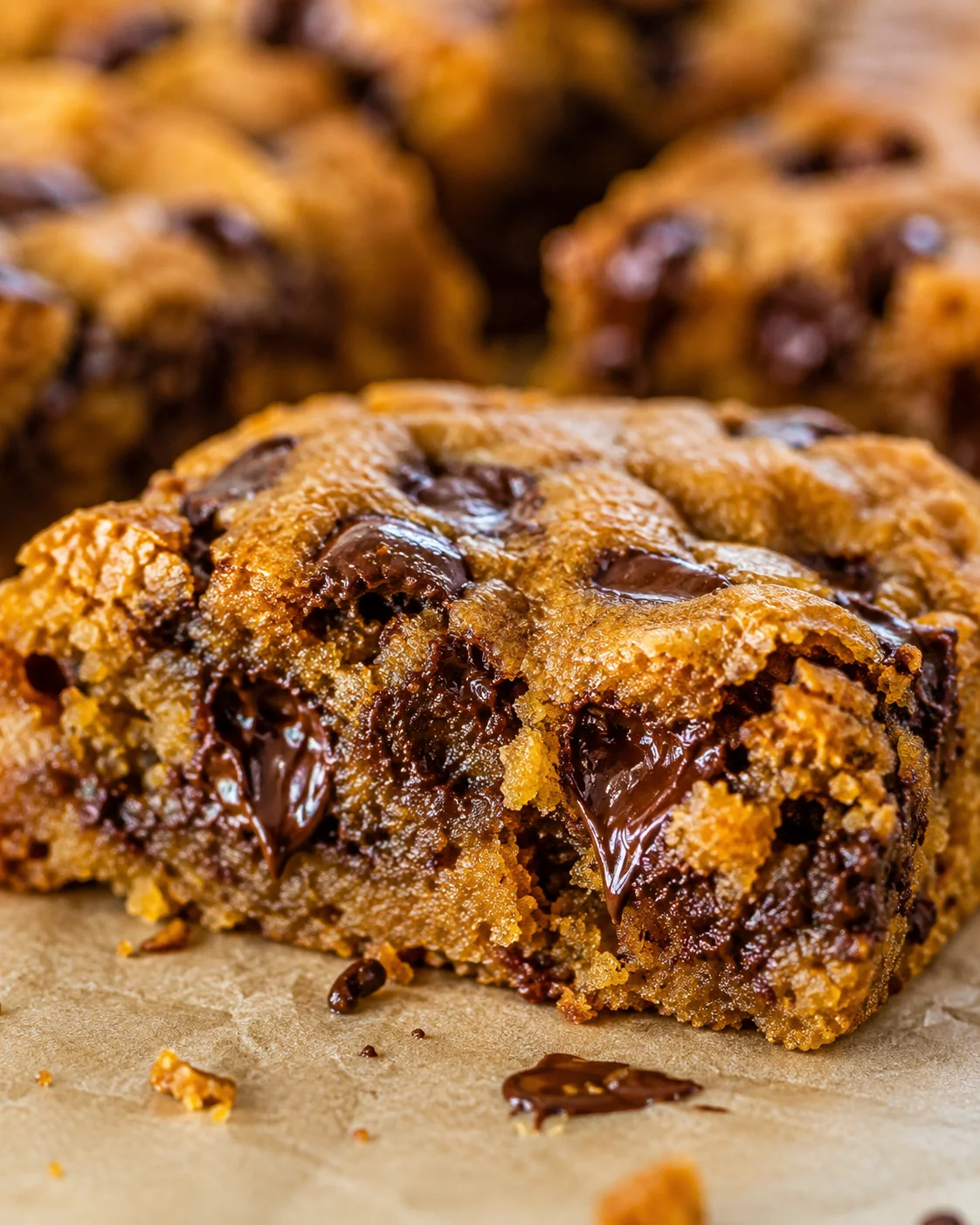 Close-up of fudgy pumpkin bars with melted chocolate chips on parchment paper.