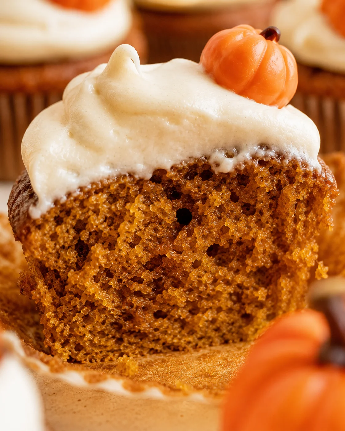 Close-up of a moist pumpkin cupcake topped with creamy frosting and a mini pumpkin decoration