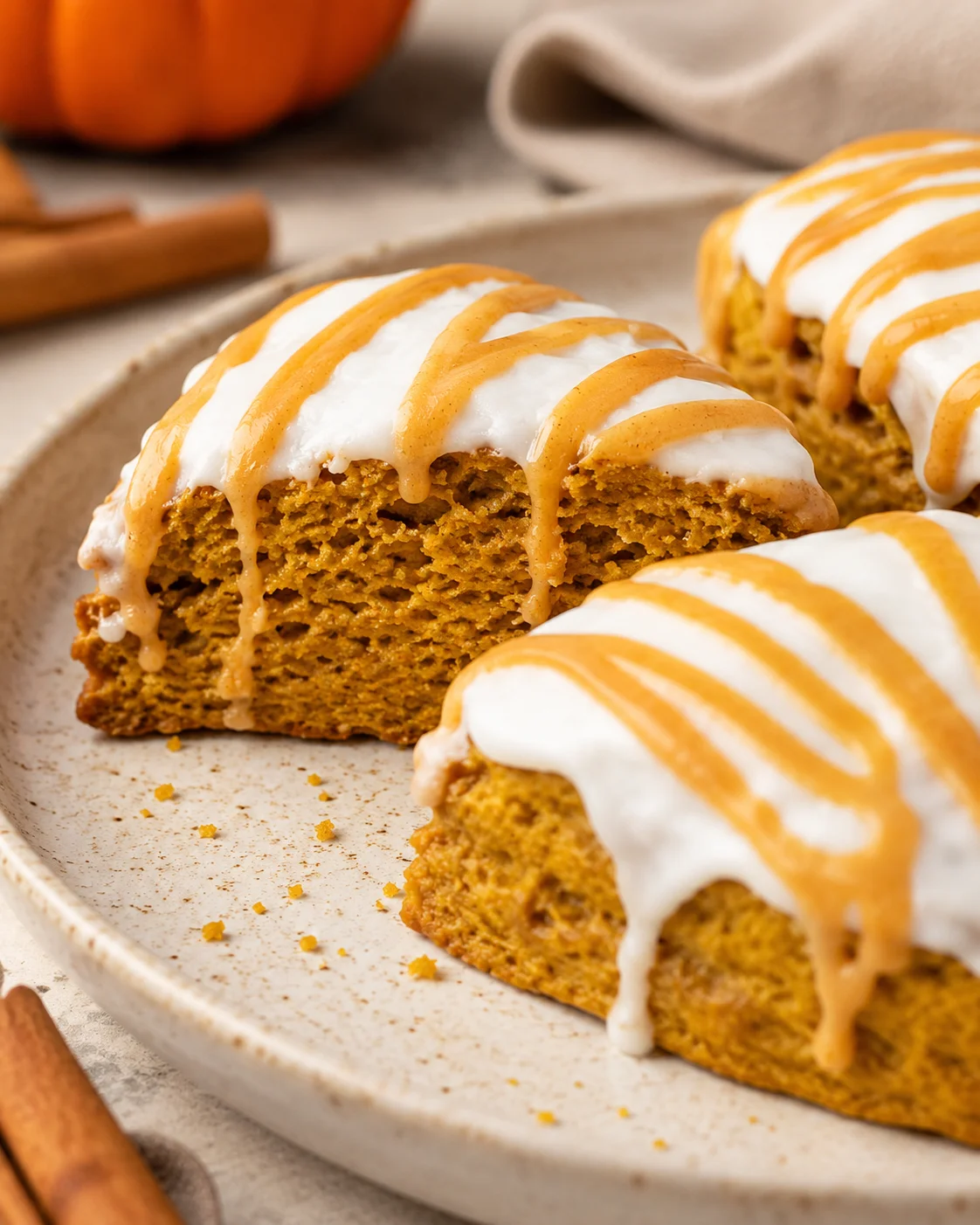 Delicious pumpkin scones topped with icing and caramel drizzle on a plate.