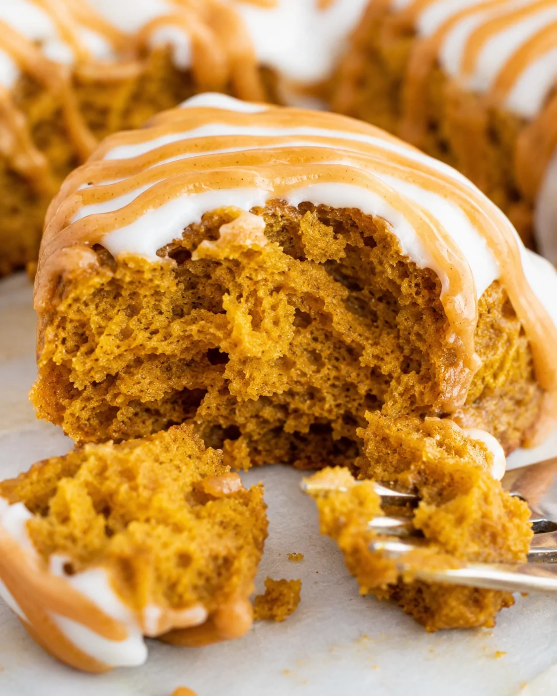 Close-up of a moist, spiced pumpkin scone topped with white icing.
