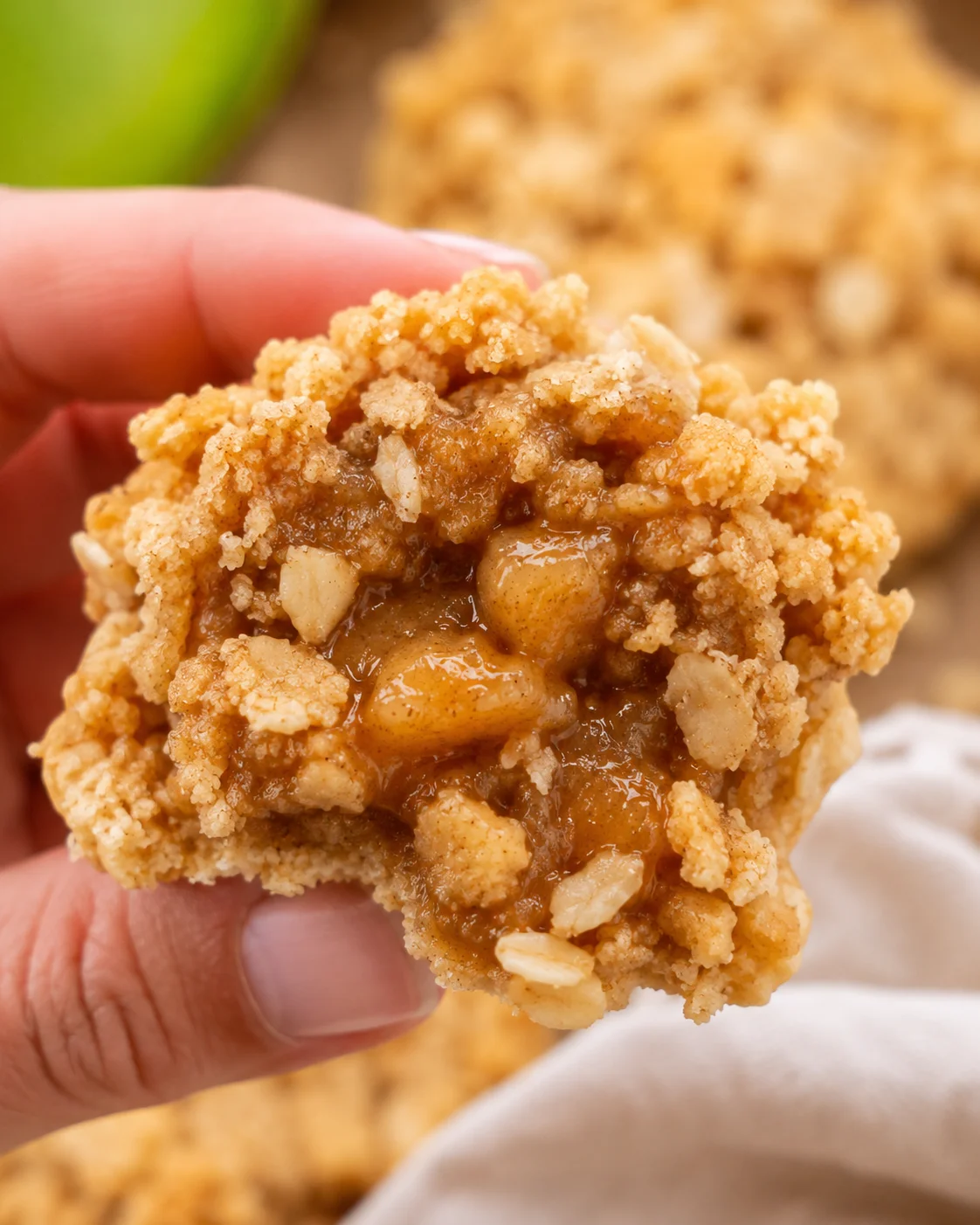 Hand holding a delicious apple crisp cookie filled with apple filling and crumb topping.