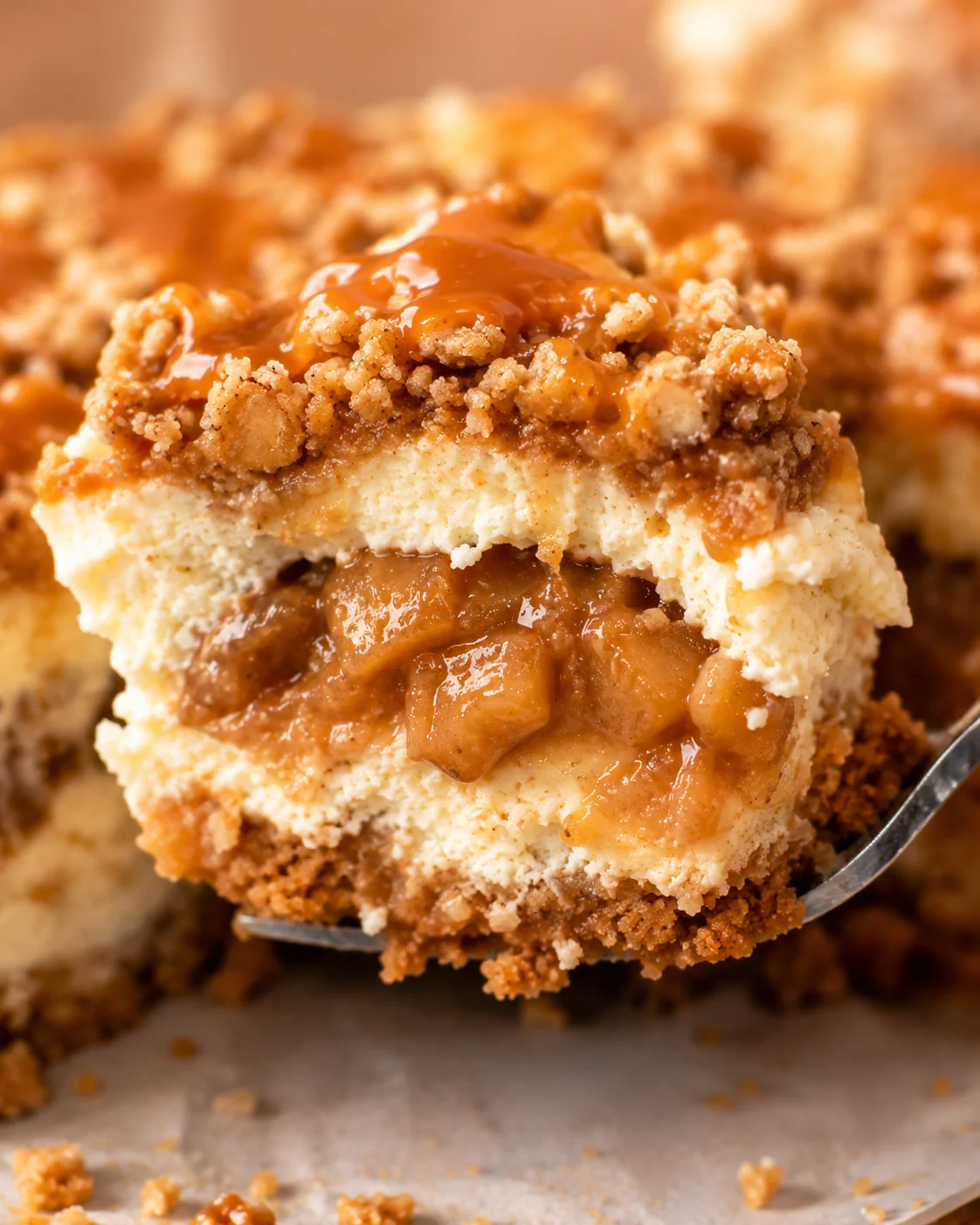 Close-up of a slice of apple crumble cheesecake with caramel topping and crumbly crust