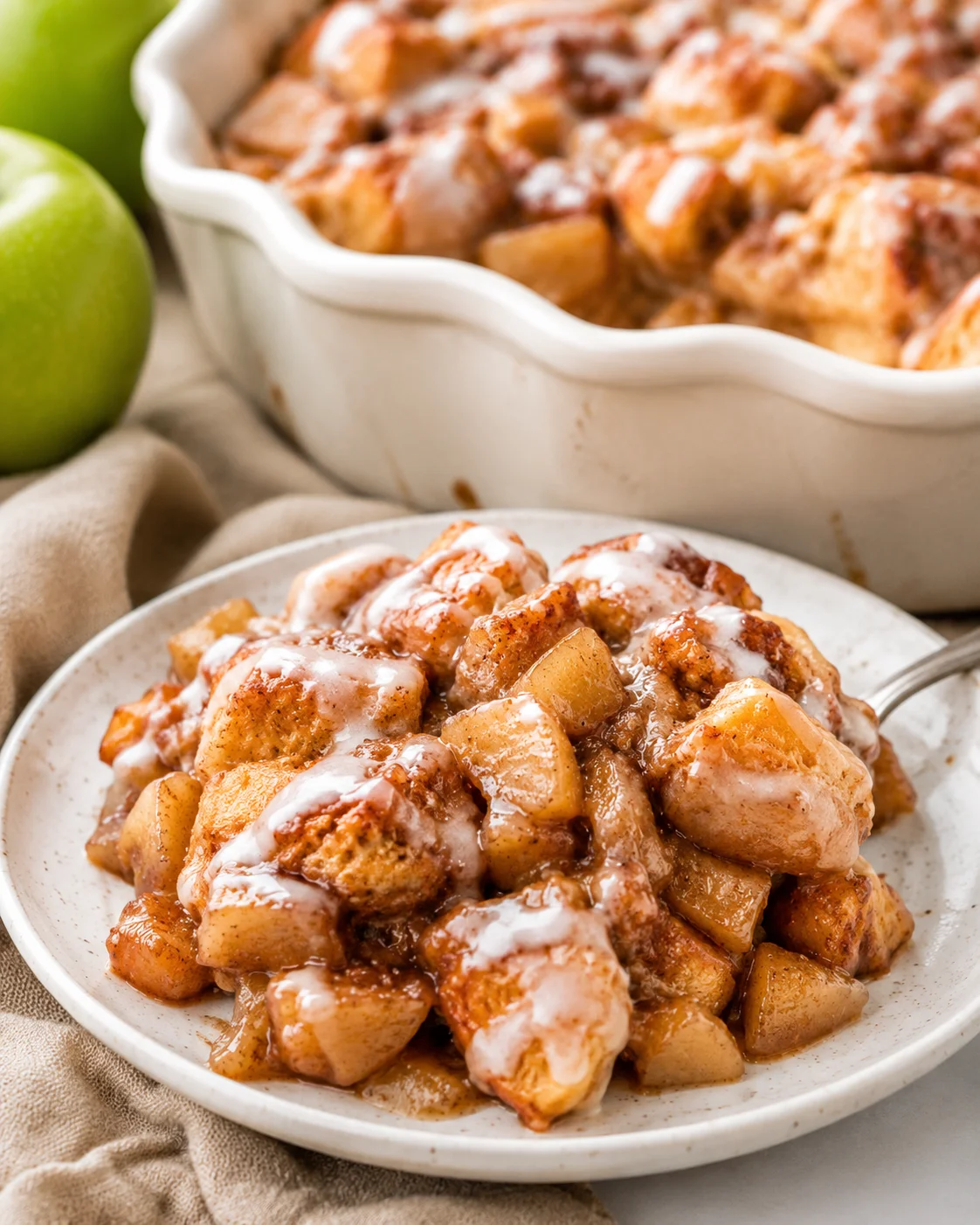Delicious apple cinnamon roll bake with apples, cinnamon, and brown sugar sauce in a white dish.
