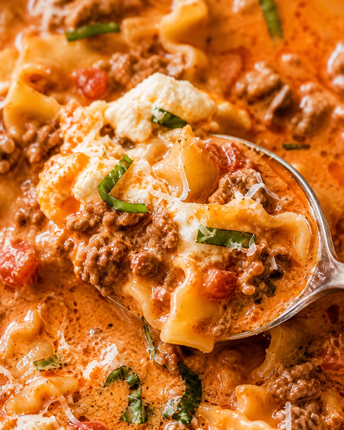Close-up of creamy lasagna soup with ground beef, cheese, and fresh basil