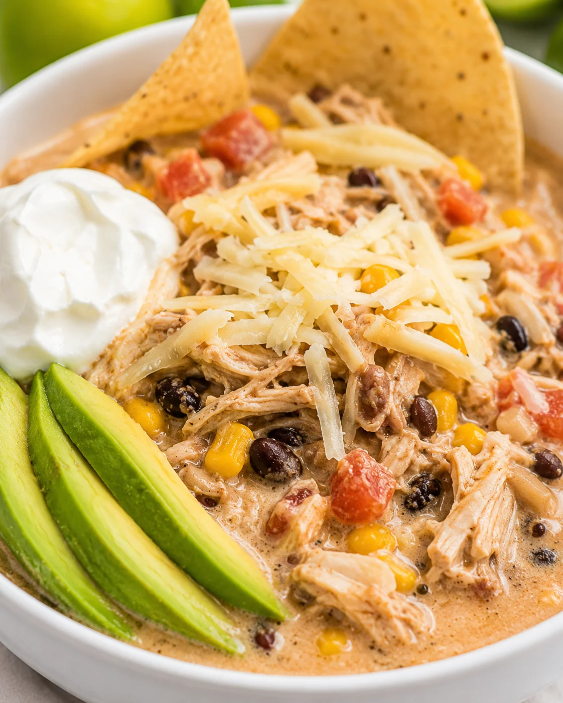 Delicious bowl of white chicken chili topped with cheese, sour cream, and avocado slices.