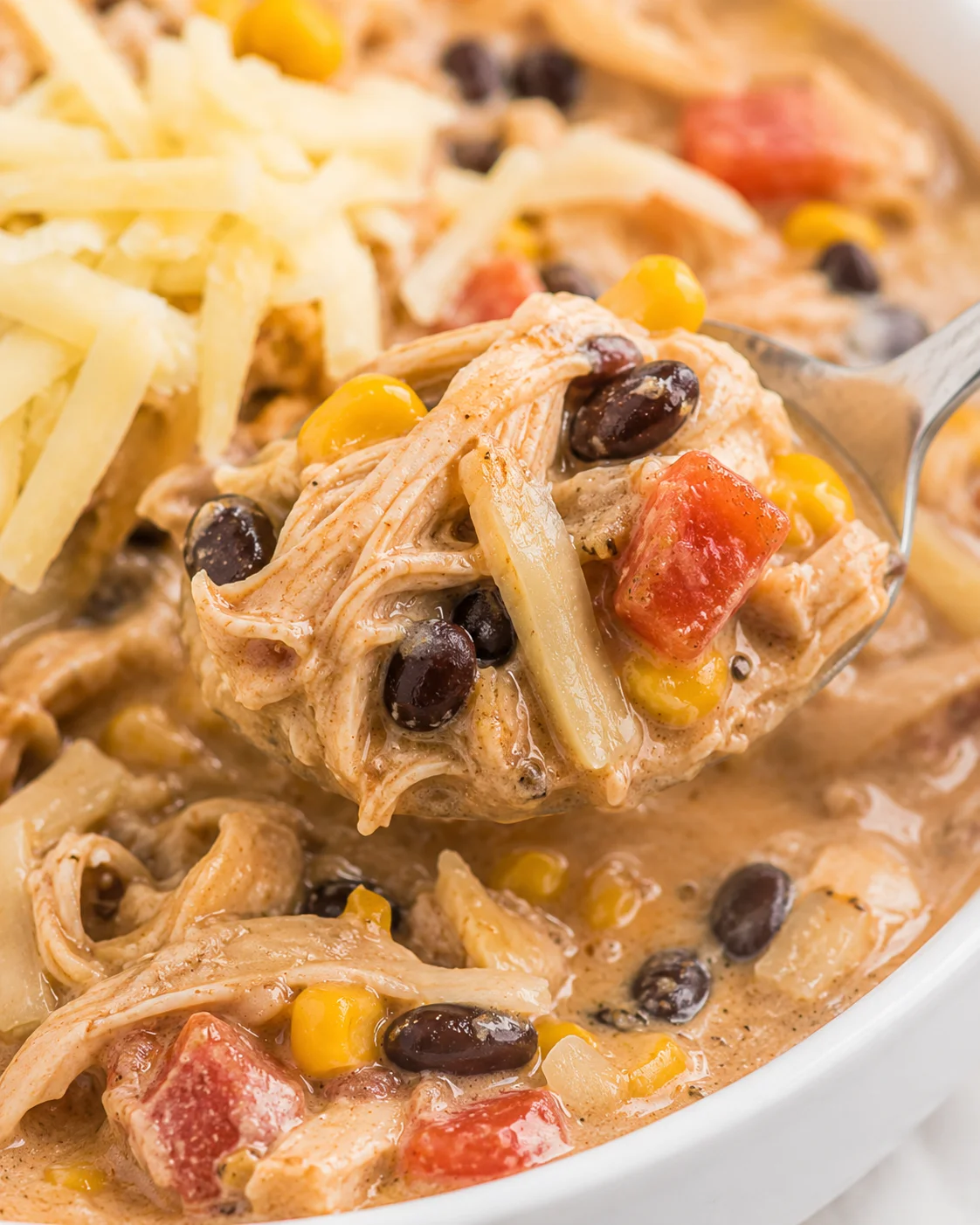 Close-up of a bowl of creamy white chicken chili with shredded chicken, beans, and corn