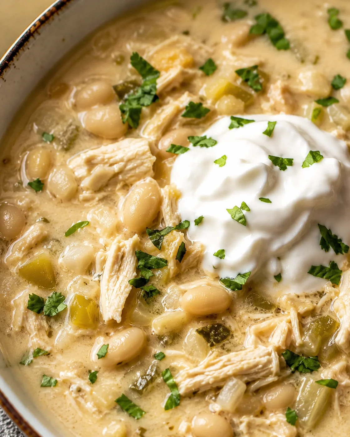 A bowl of creamy white chicken chili topped with sour cream and herbs.