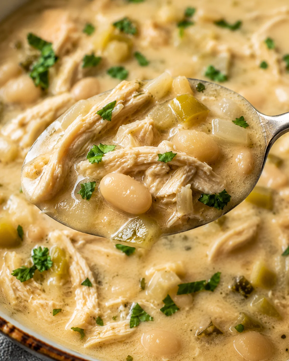 A spoonful of creamy white chicken chili with chicken, beans, and herbs.