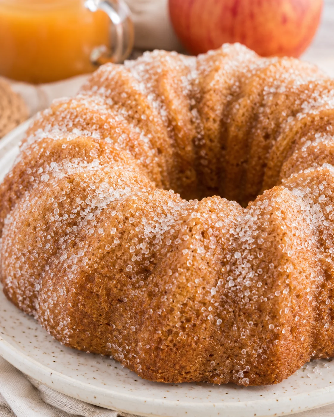 Whole apple cider donut bundt cake coated in cinnamon sugar on a plate