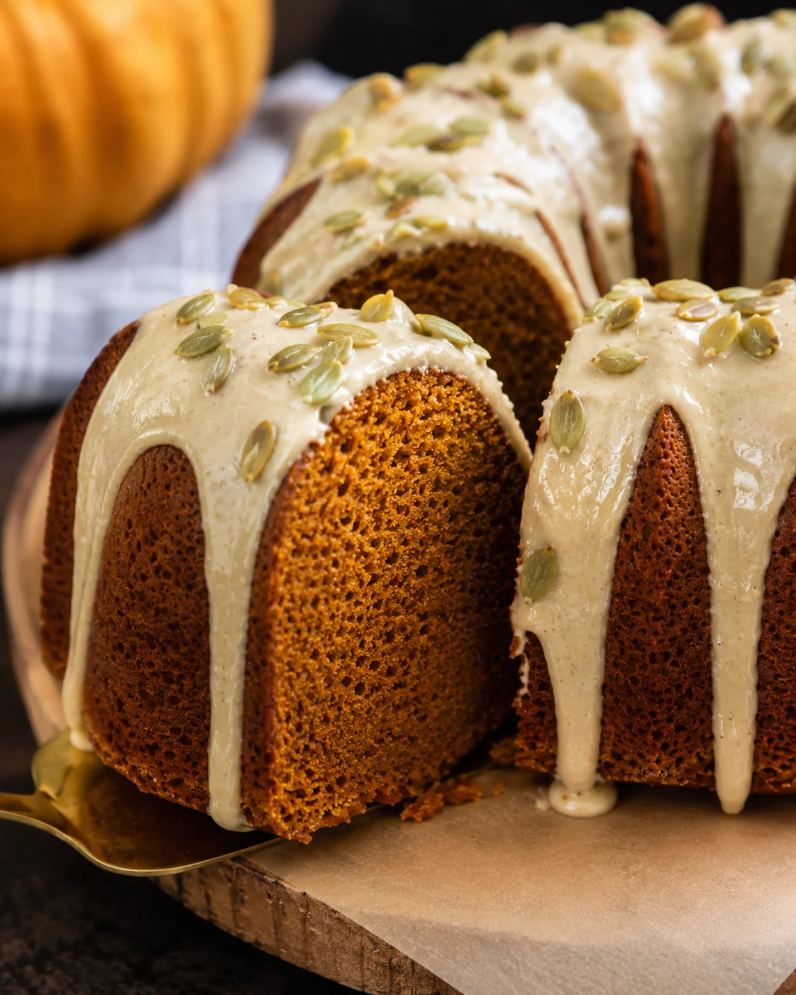 Close-up of a moist pumpkin bundt cake drizzled with maple glaze and topped with pumpkin seeds.